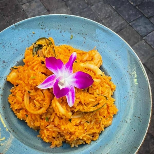 Peruvian arroz con mariscos, orange seafood rice with squid, mussels, and a purple orchid garnish.