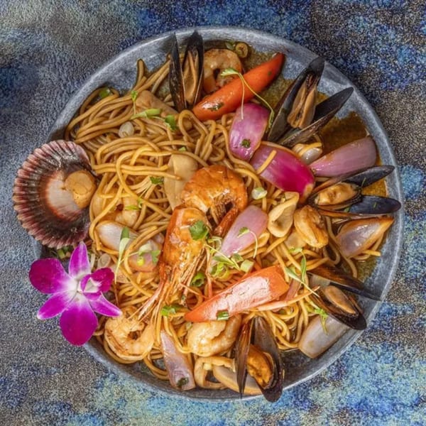 Peruvian seafood noodles with shrimp, mussels, scallops, red onion, and bell pepper, garnished with an orchid.