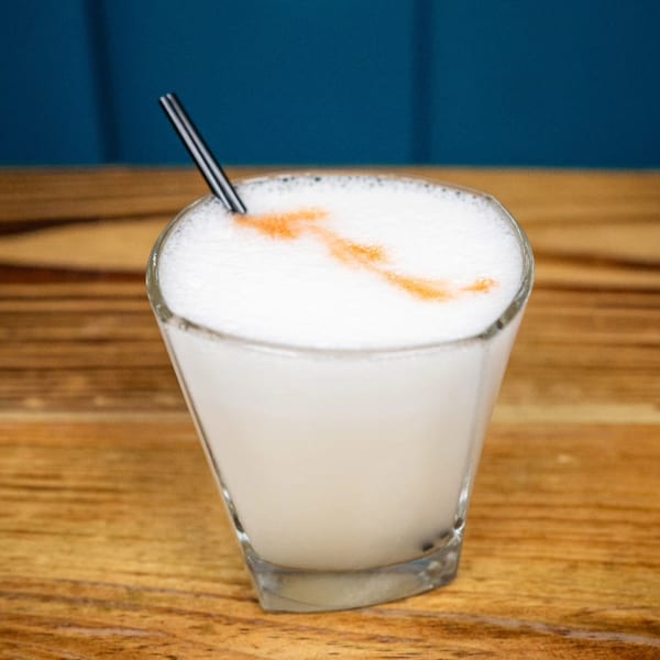 Peruvian Pisco Sour cocktail with a foamy top and cinnamon swirl, served in a glass with a straw.