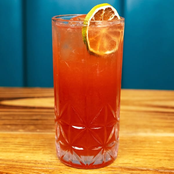 A tall glass of red Peruvian cocktail with ice and a lime slice on a wooden table.
