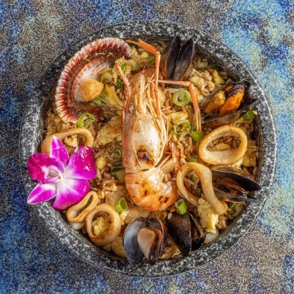 Peruvian arroz con mariscos, featuring shrimp, mussels, squid, and a scallop, garnished with an orchid.