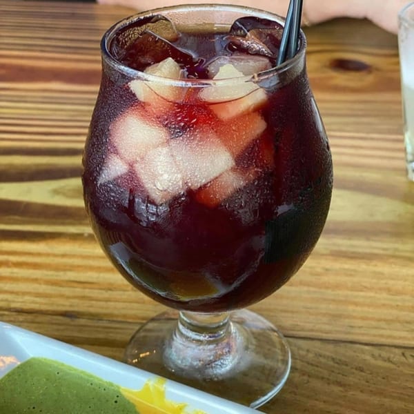 A glass of Divino Ceviche's red sangria with ice and fruit on a wooden table.
