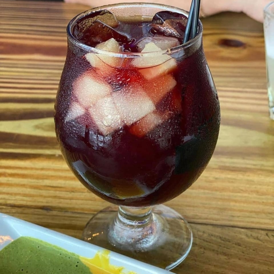 A glass of Divino Ceviche's red sangria with ice and fruit on a wooden table.