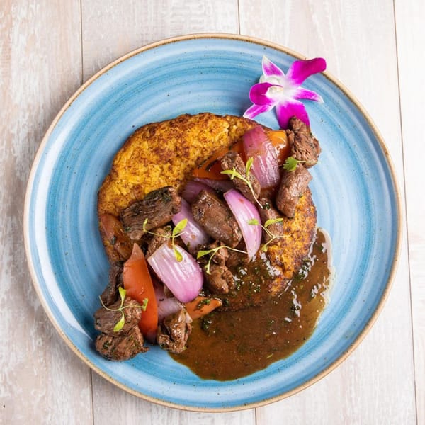 Peruvian Lomo Saltado with beef, red onions, tomatoes, and a rich sauce, garnished with an orchid.