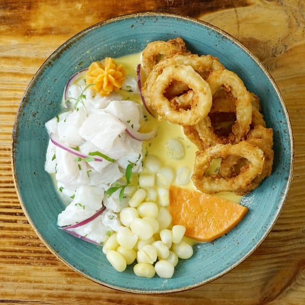 Peruvian ceviche with fried calamari, corn, sweet potato, and red onion on a blue plate.