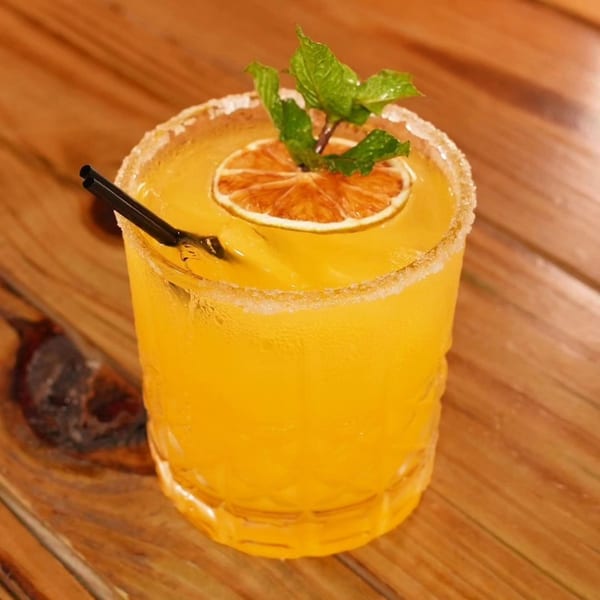 A Peruvian cocktail, yellow with a sugared rim, garnished with a dried orange slice and mint.