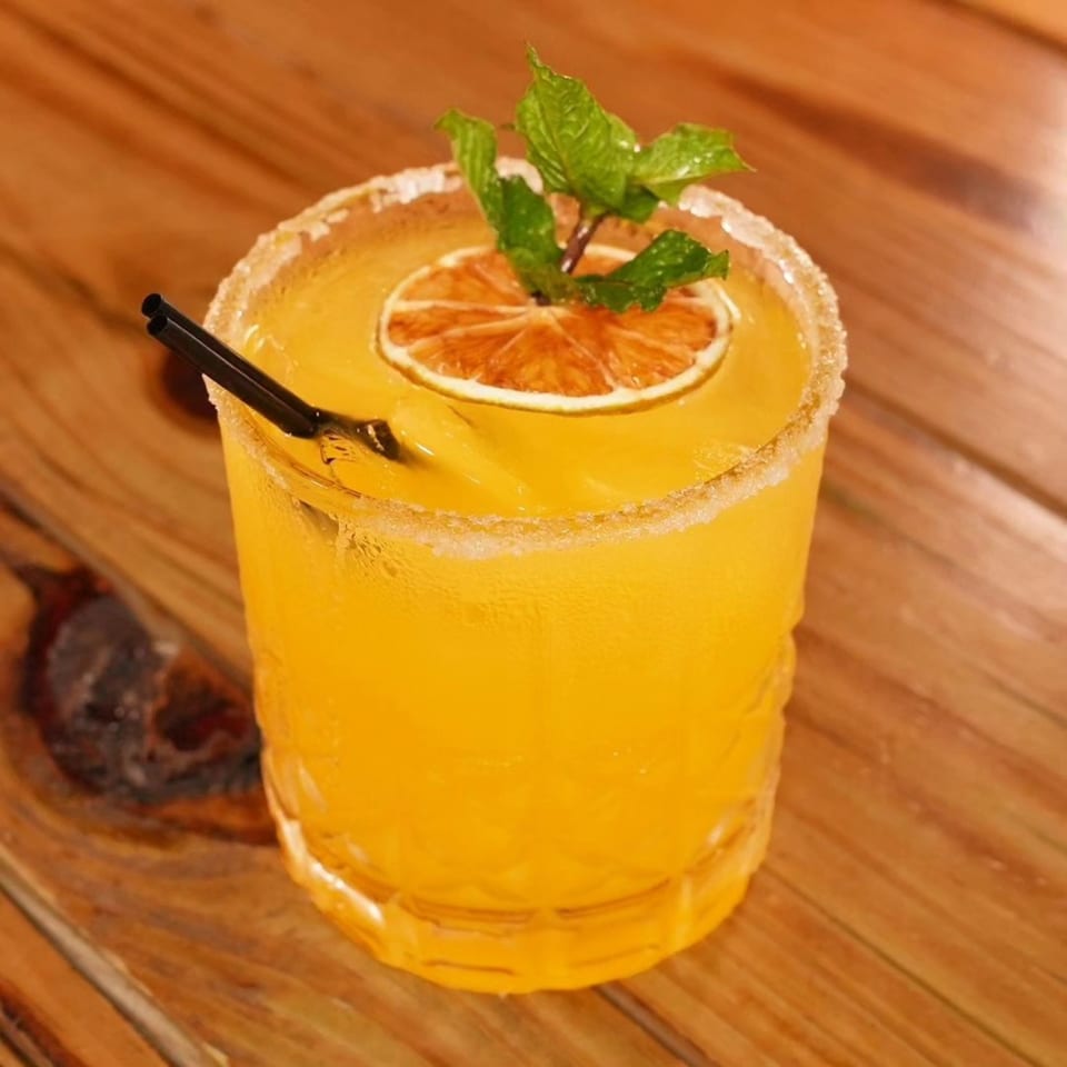 A Peruvian cocktail, yellow with a sugared rim, garnished with a dried orange slice and mint.