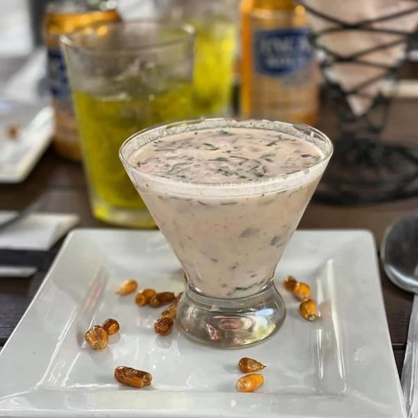 Peruvian leche de tigre cocktail in a martini glass, garnished with toasted corn kernels on a white plate.