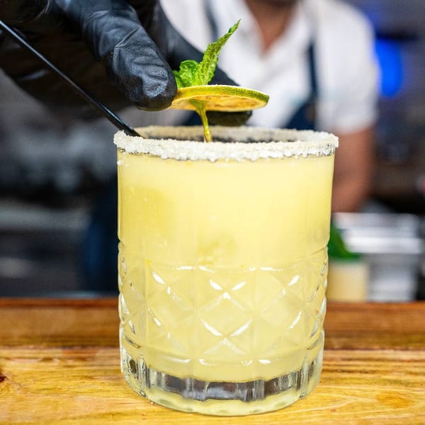 A hand in a black glove garnishes a Peruvian cocktail with a lime slice and mint.