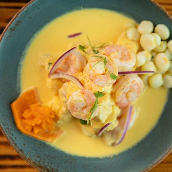 Peruvian shrimp ceviche in a yellow sauce with red onions, corn, and sweet potato.