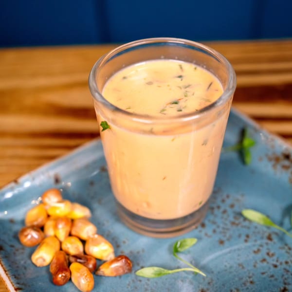 Peruvian leche de tigre in a glass with toasted corn and herbs on a blue plate.