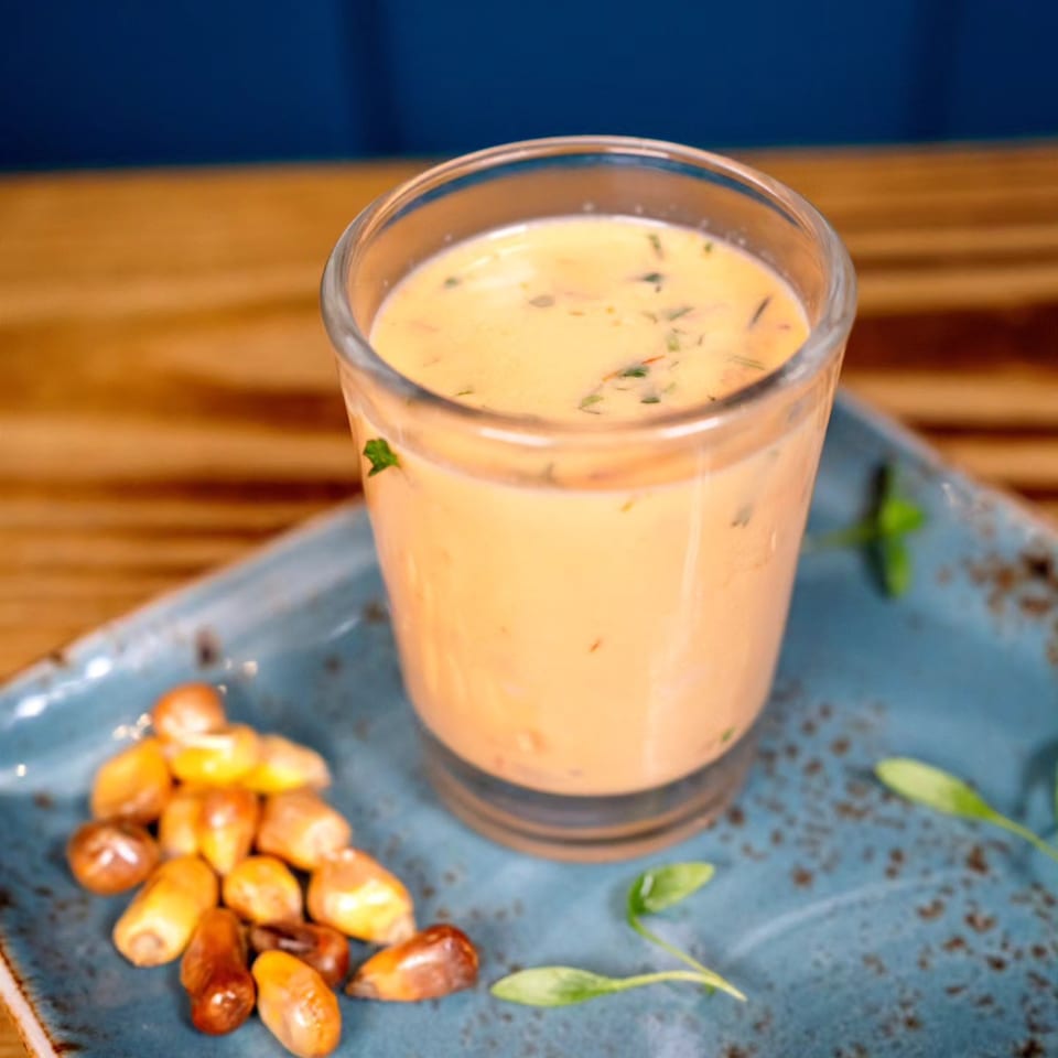 Peruvian leche de tigre in a glass with toasted corn and herbs on a blue plate.