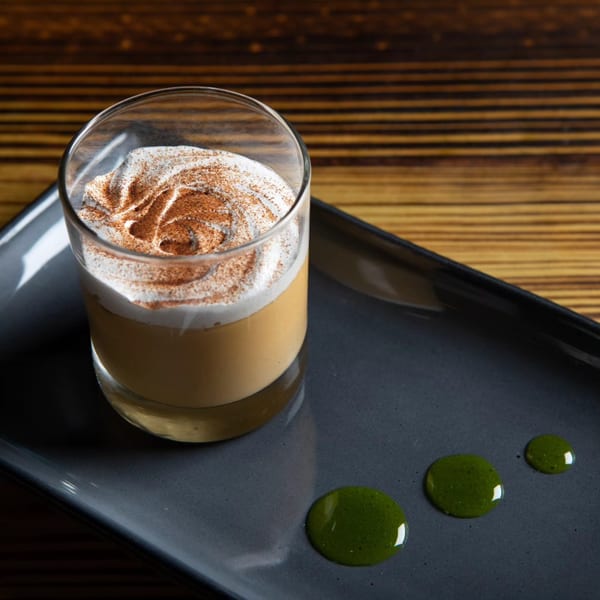 Peruvian dessert in a glass with whipped cream and cinnamon, garnished with green sauce on a dark plate.
