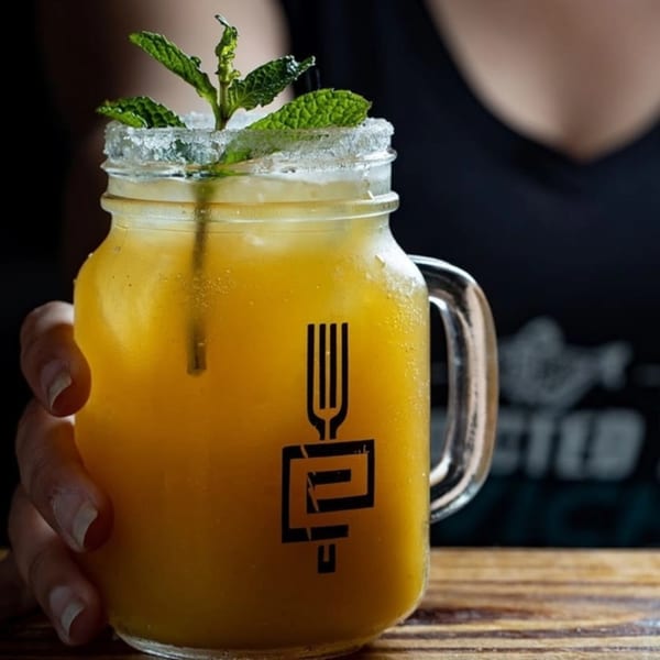 Hand holding a mason jar of yellow Peruvian drink with mint and a sugar-rimmed glass.